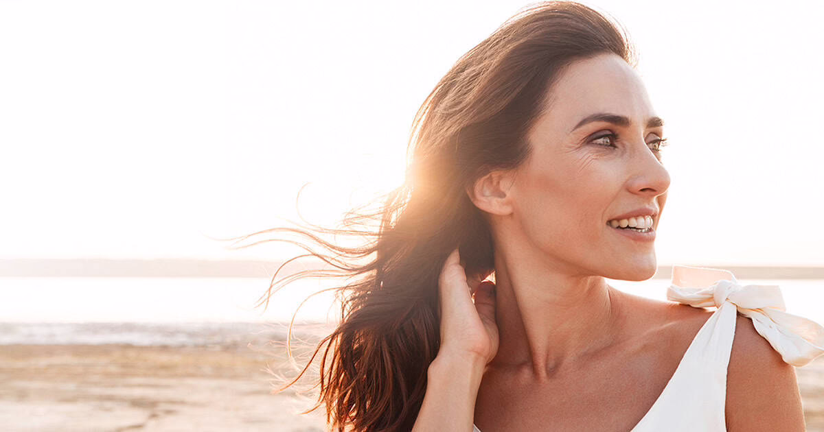 woman-at-beach-looking-happy Woman at beach, looking over shoulder and smiling