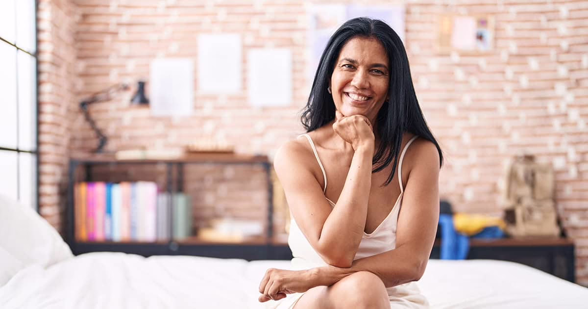 Milli woman sitting on edge of bed 1200w vaginal dryness remedies woman sitting on edge of bed smiling